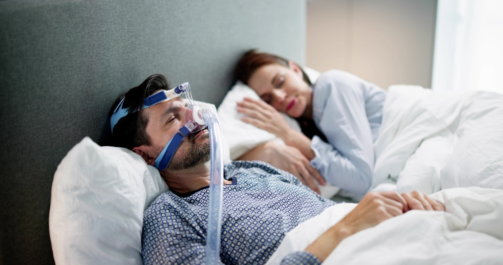 Man wearing a CPAP mask sleeping next to a woman in bed